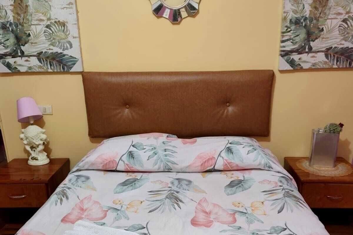 A bedroom with a floral bedspread, a round mirror, and two wall art pieces.