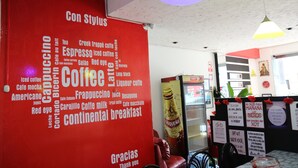 A coffee shop interior with a red wall featuring a coffee-related word cloud and a sign that reads "Gracias Thank you." - Stylus Hotel (Iquitos)