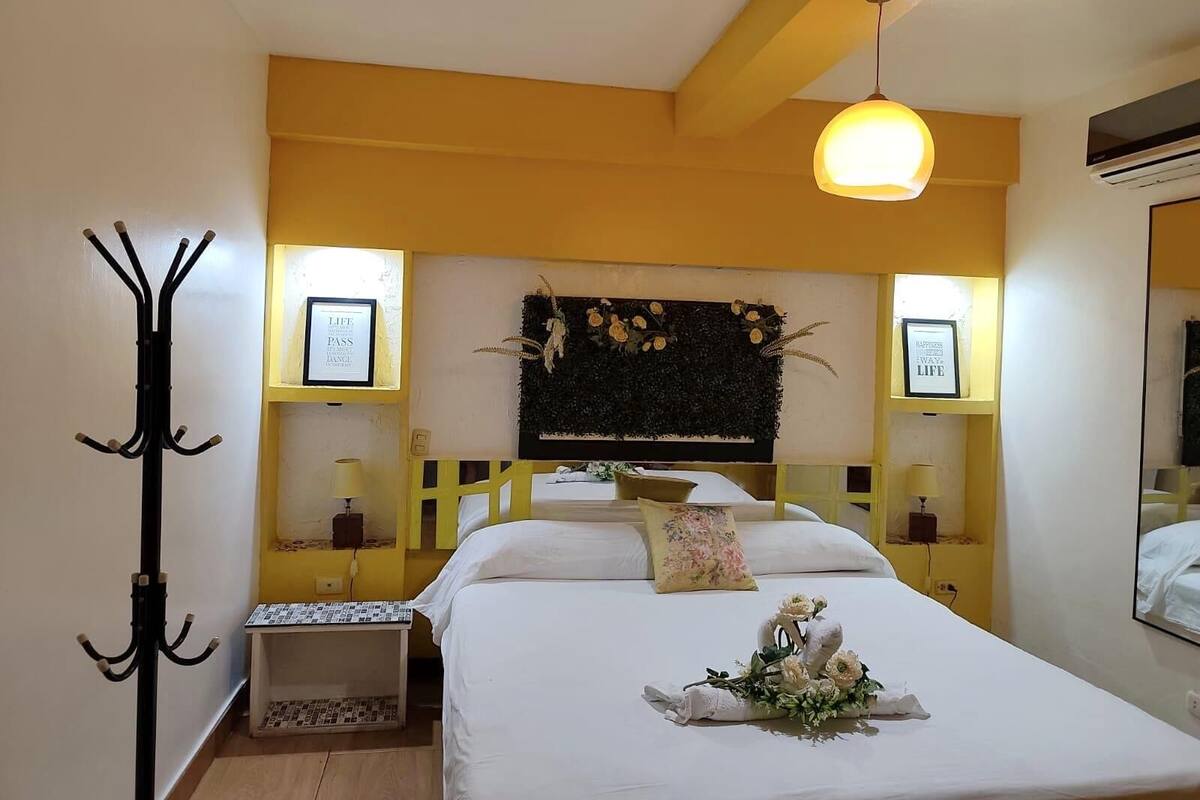 A hotel room with a bed, a coat rack, a small table, and a decorative wall panel.