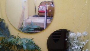 A room with a large round mirror, a smaller mirror, a potted plant, and a small table with a vase of flowers. - Stylus Hotel (Iquitos)