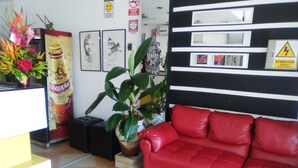 A reception area with a red sofa, a potted plant, and framed artwork on the wall. - Stylus Hotel (Iquitos)