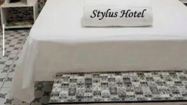 A hotel room with a bed, two bedside tables with lamps, a wall with Eiffel Tower silhouette, and a pillow with 'Stylus Hotel' text. - Stylus Hotel (Iquitos)