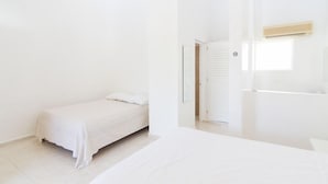 A minimalist bedroom with a single bed, a small bedside table, and a door leading to a bathroom. - Northway's Hotel Monte Cristo (Cabarete)