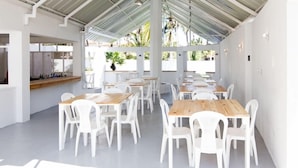 A spacious indoor dining area with white chairs and wooden tables, large windows, and a view of palm trees outside. - Northway's Hotel Monte Cristo (Cabarete)
