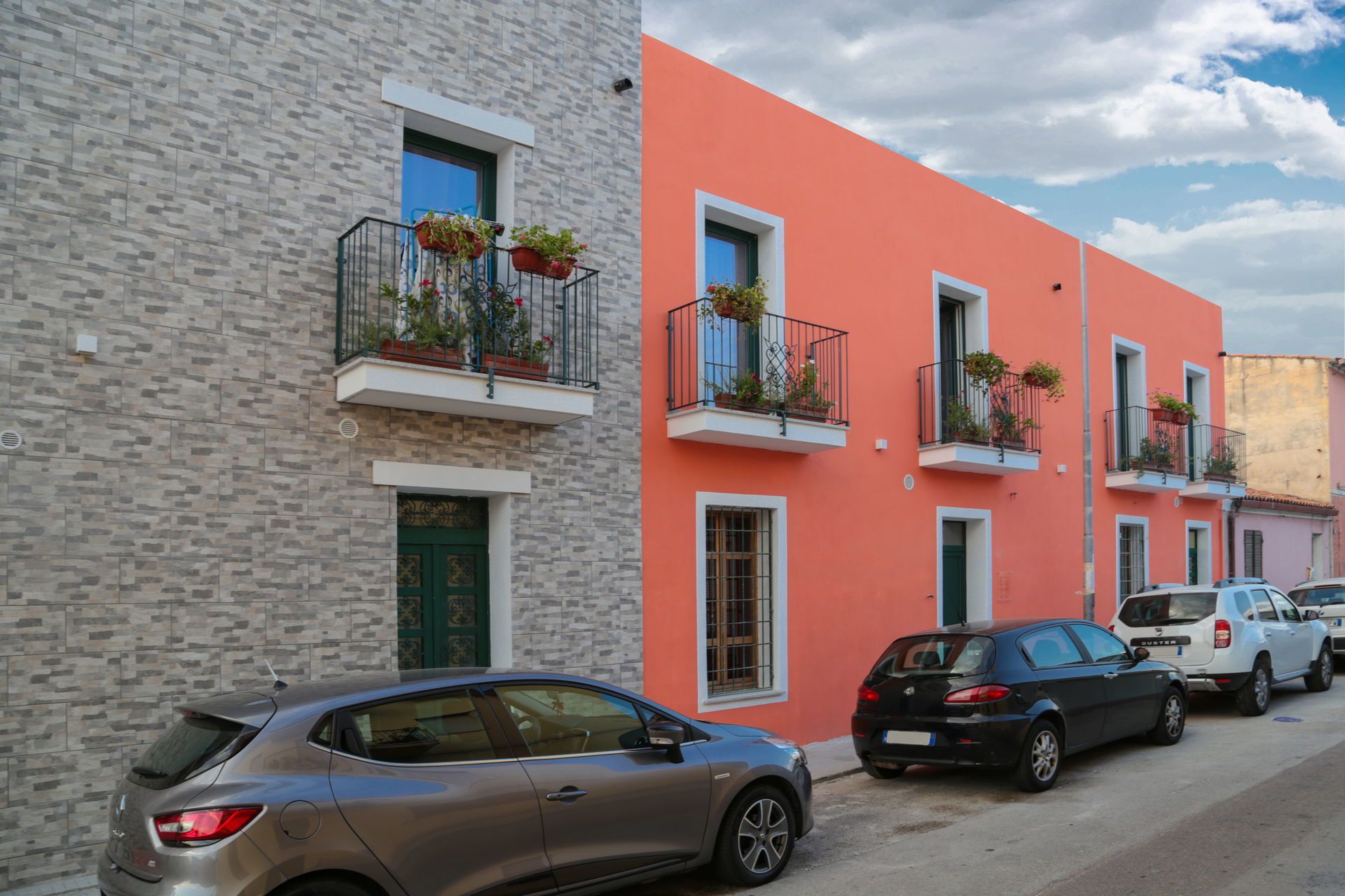 A row of two-story buildings with balconies, parked cars, and a clear sky.