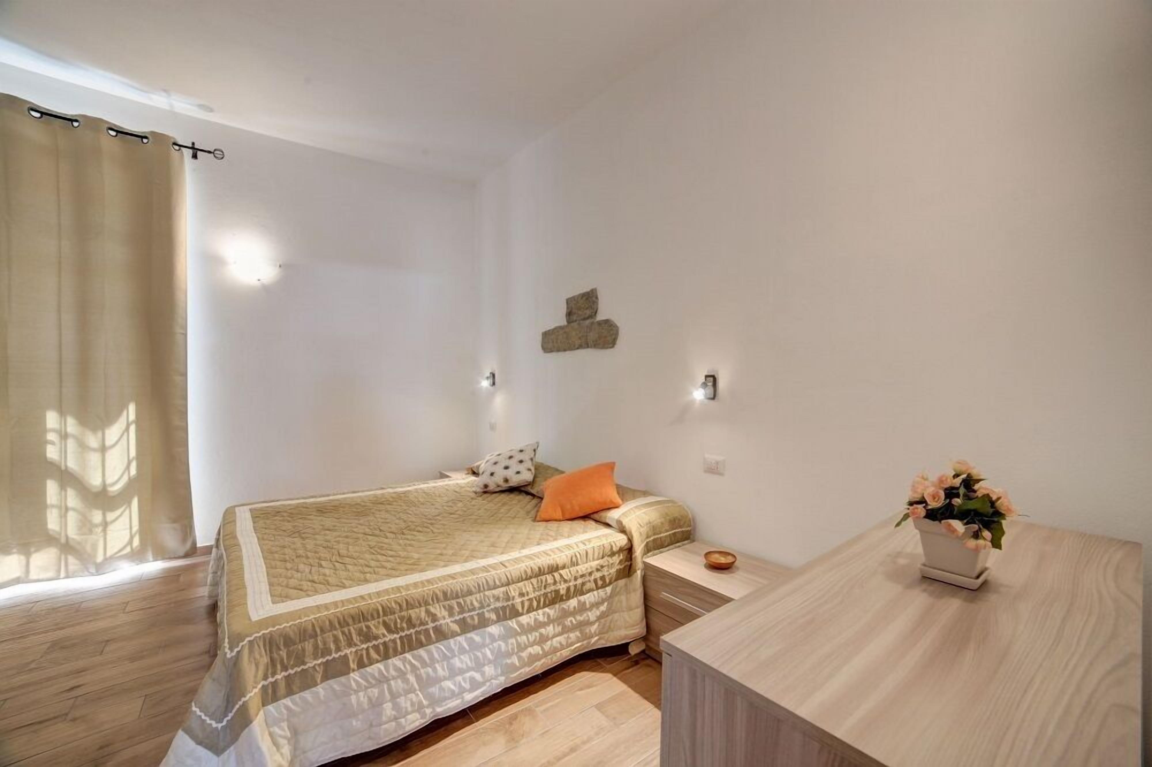 A bedroom with a bed, a nightstand, a small table, and a potted plant.