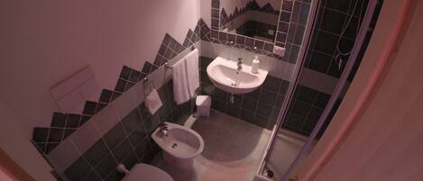 A compact bathroom with a toilet, bidet, sink, and a shower area.