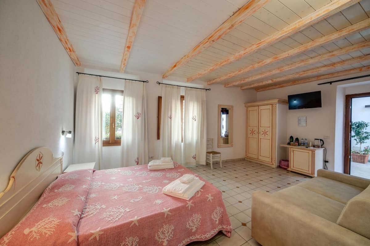 A bedroom with a bed, a sofa, a TV, a wardrobe, and a bathroom visible through an open door.