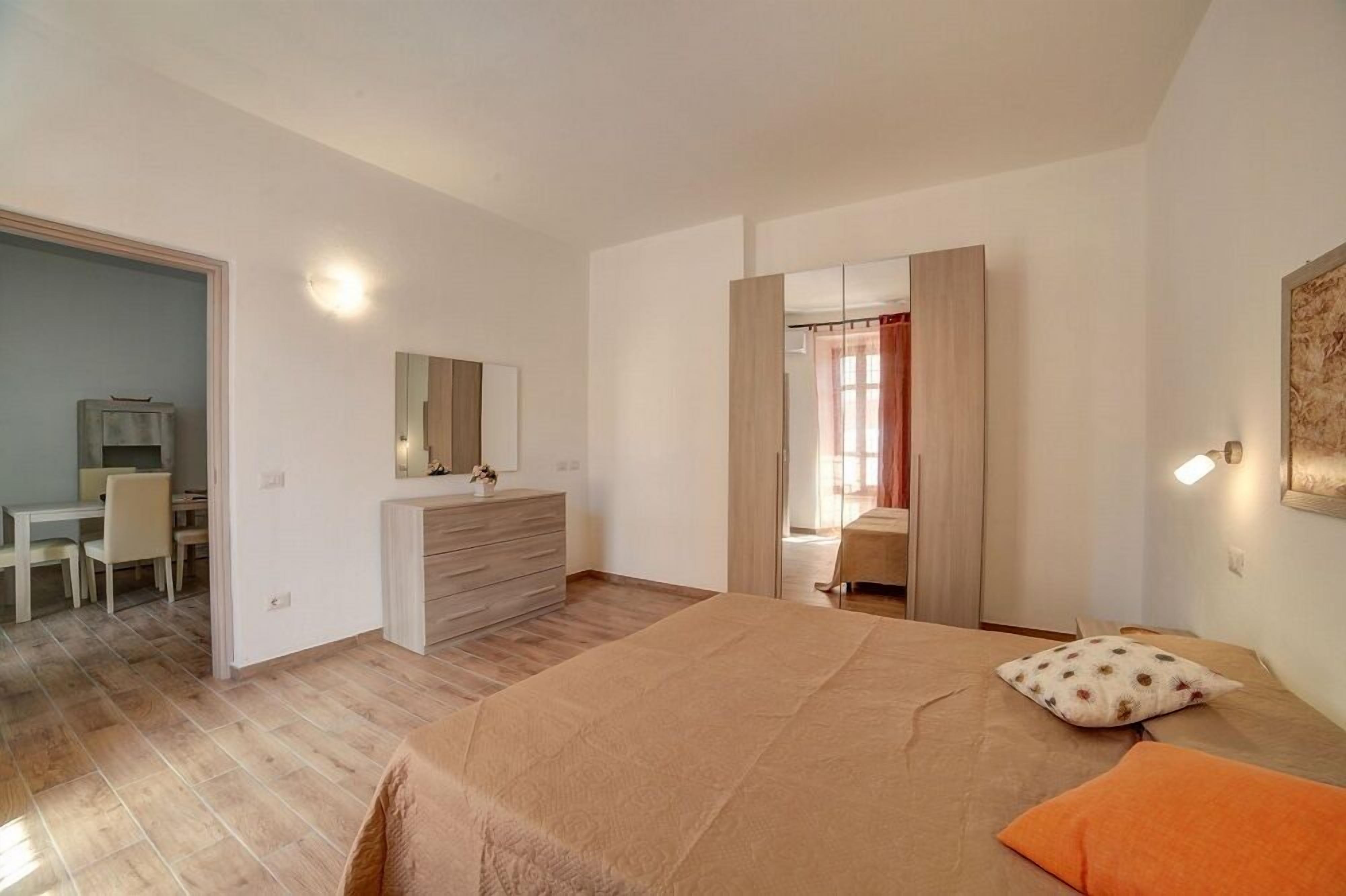 A bedroom with a bed, a dresser, a mirror, and a desk with chairs.