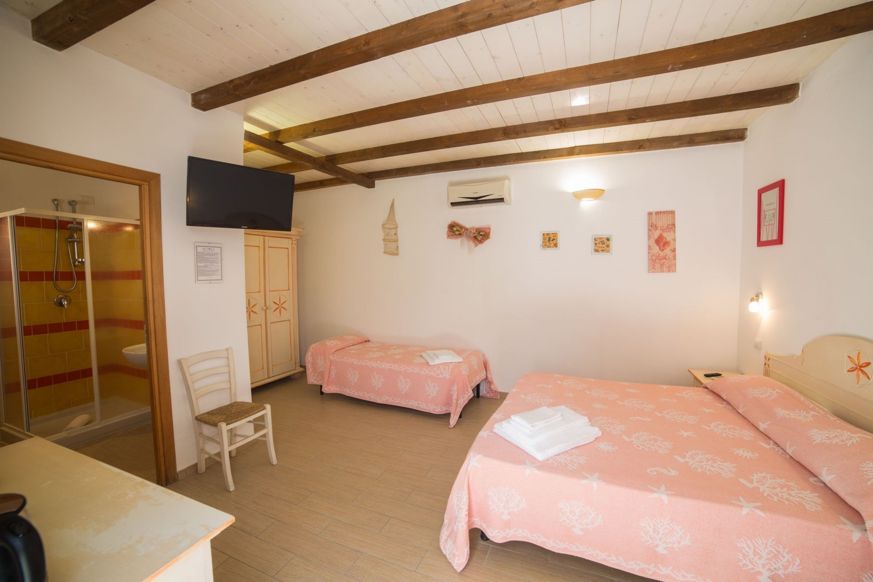 Een slaapkamer met twee bedden, een houten plafond, een televisie en een douche.