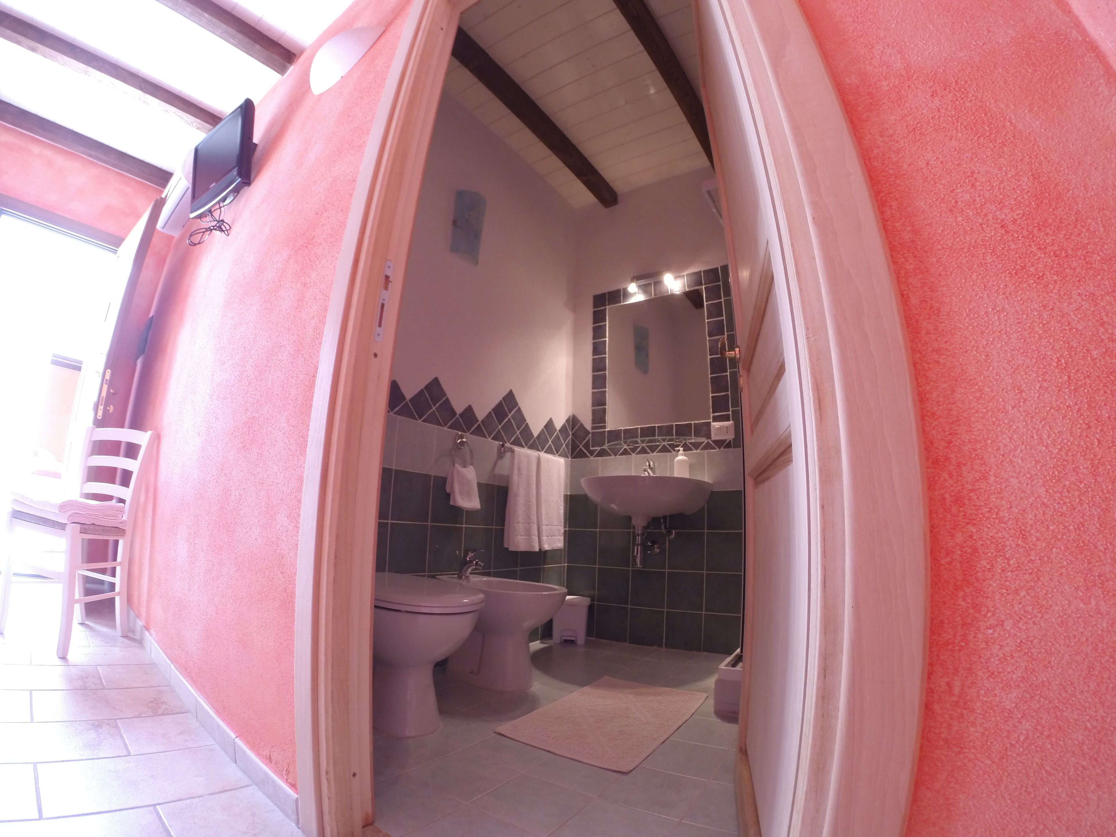 A bathroom with a pink wall, a sink, a toilet, and a bidet.