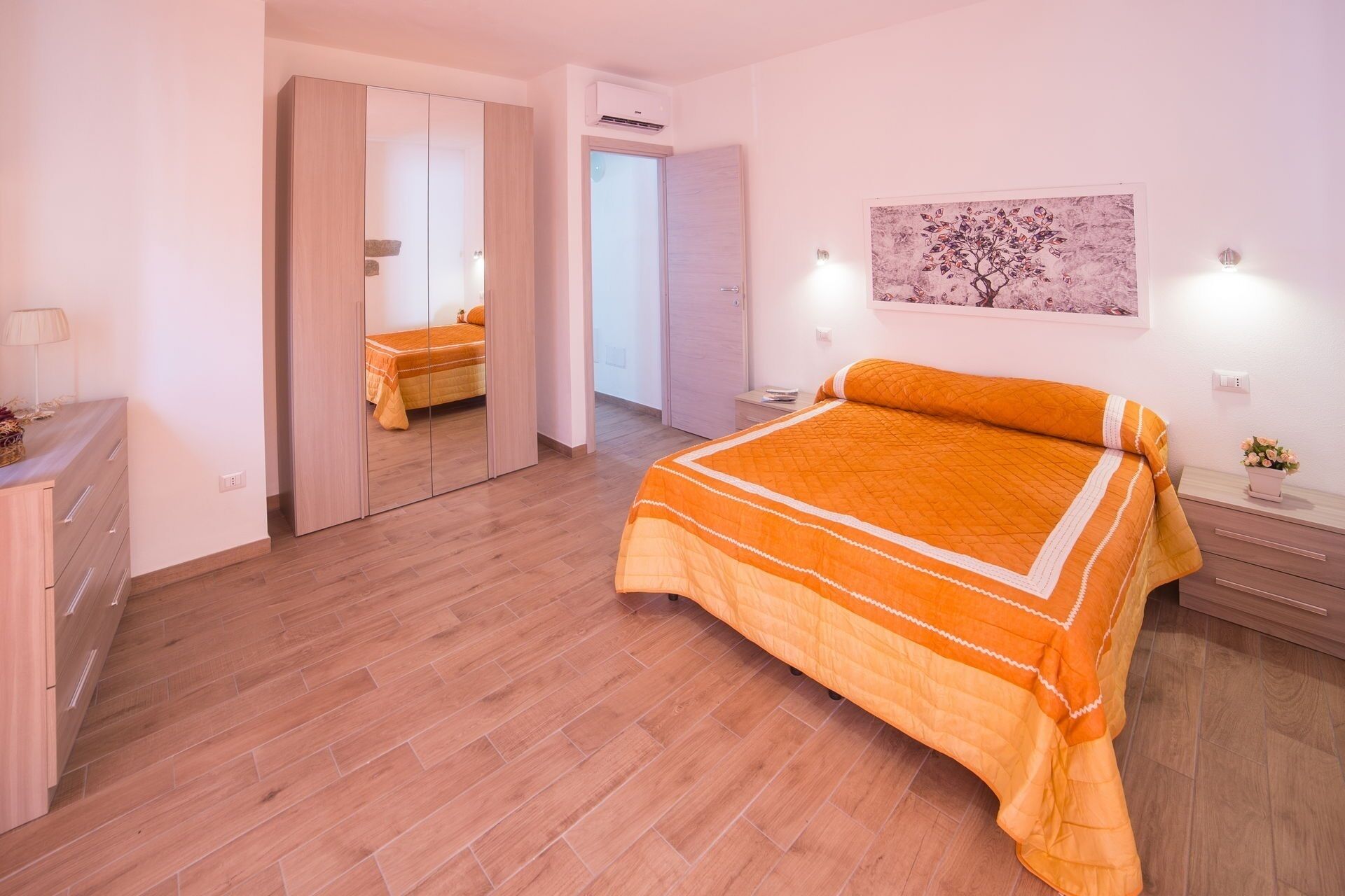 Ein Schlafzimmer mit einem großen Bett, Holzboden, einem Kleiderschrank, einem Nachttisch mit Lampe und einer Wand-Klimaanlage.
