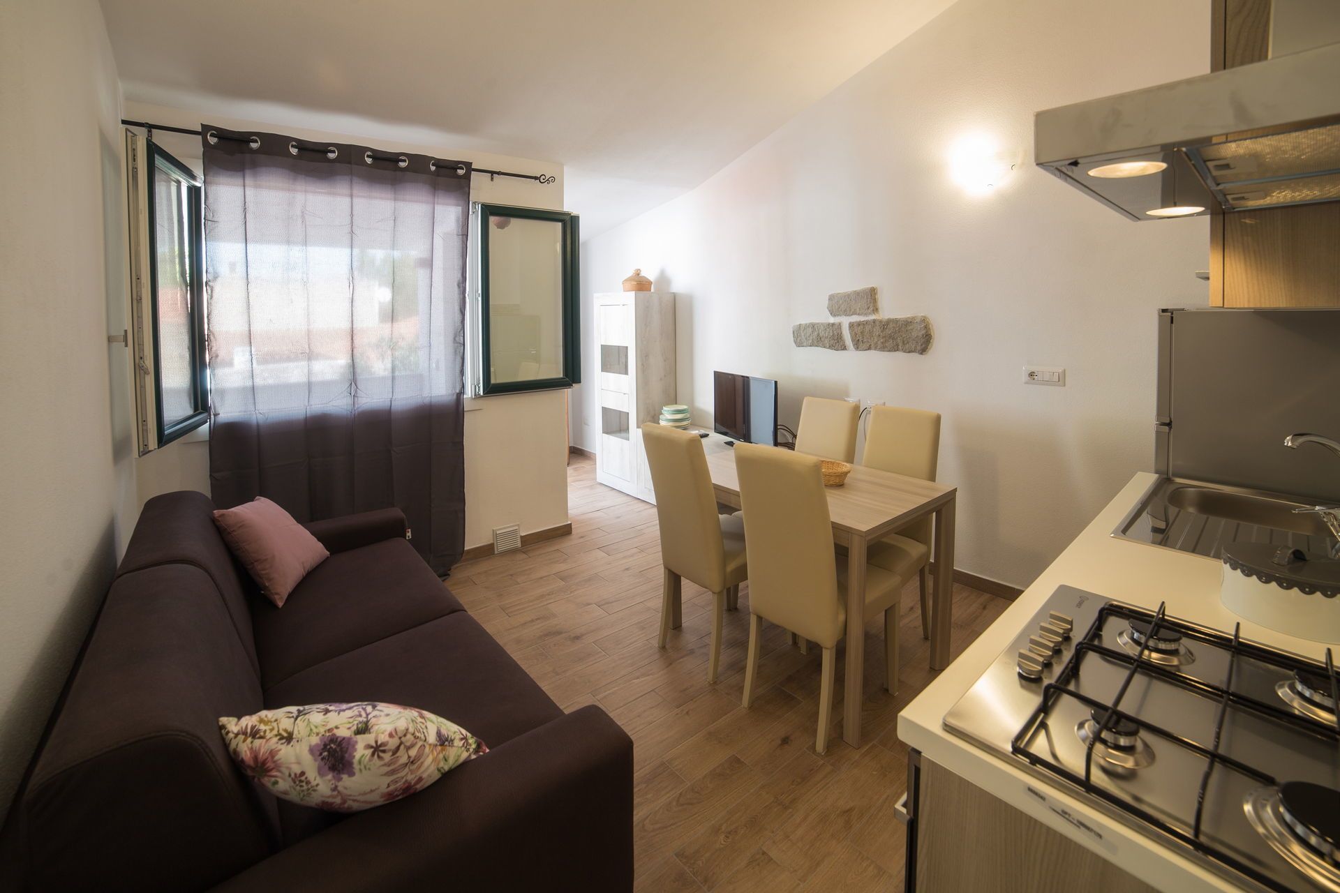 Een ruimtelijk ingerichte leefruimte met een bank, eettafel, stoelen, een televisie en een keukenhoek met een fornuis.