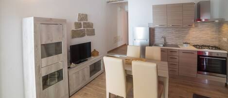 A modern kitchen with a built-in oven, a stove, and a sink. There is a dining area with a table and chairs.