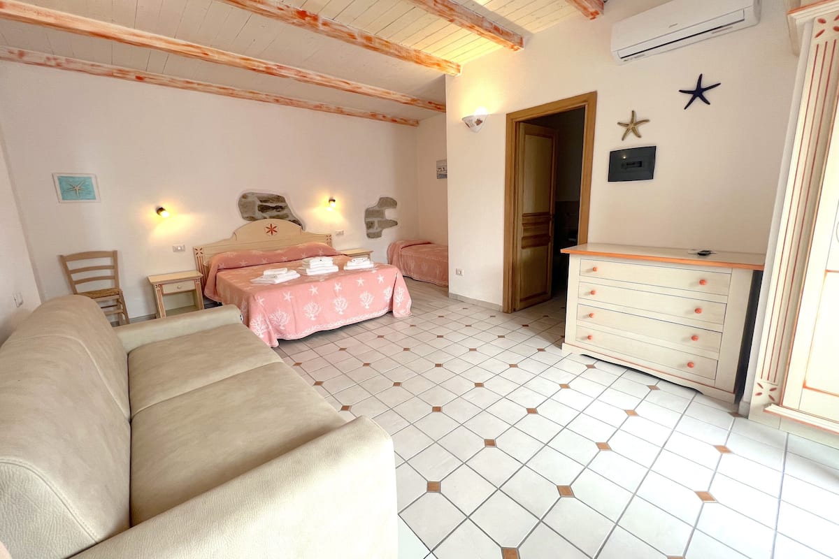 A bedroom with a bed, a sofa, a dresser, and a tiled floor.