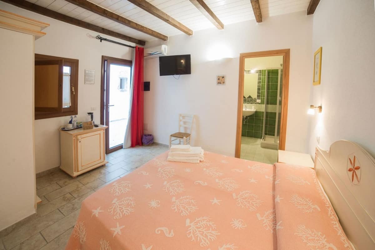 A bedroom with a bed, a TV, a wooden cabinet, and a bathroom visible through an open door.