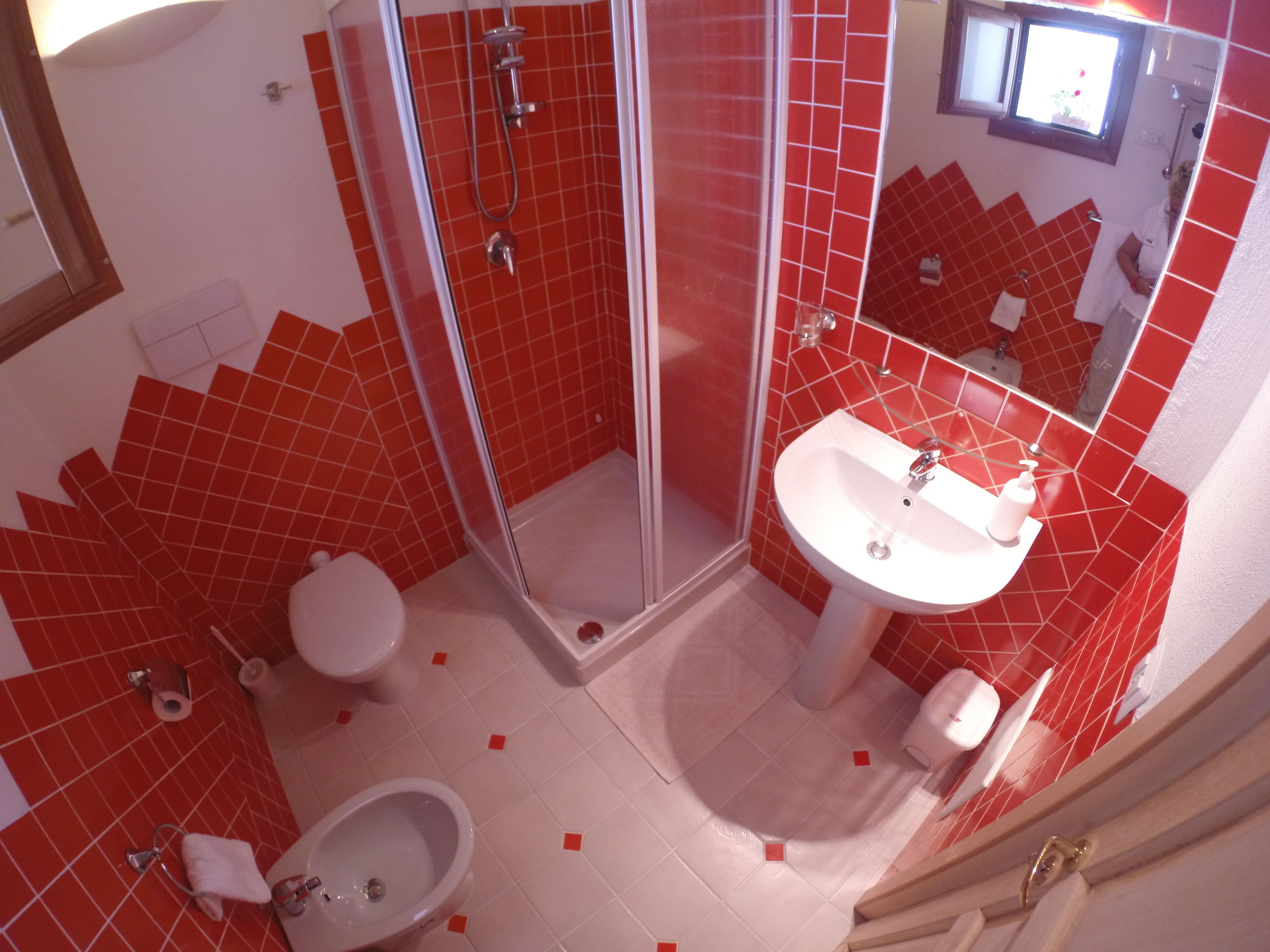 Une salle de bain avec des carreaux rouges, une douche en verre, un lavabo et des toilettes.