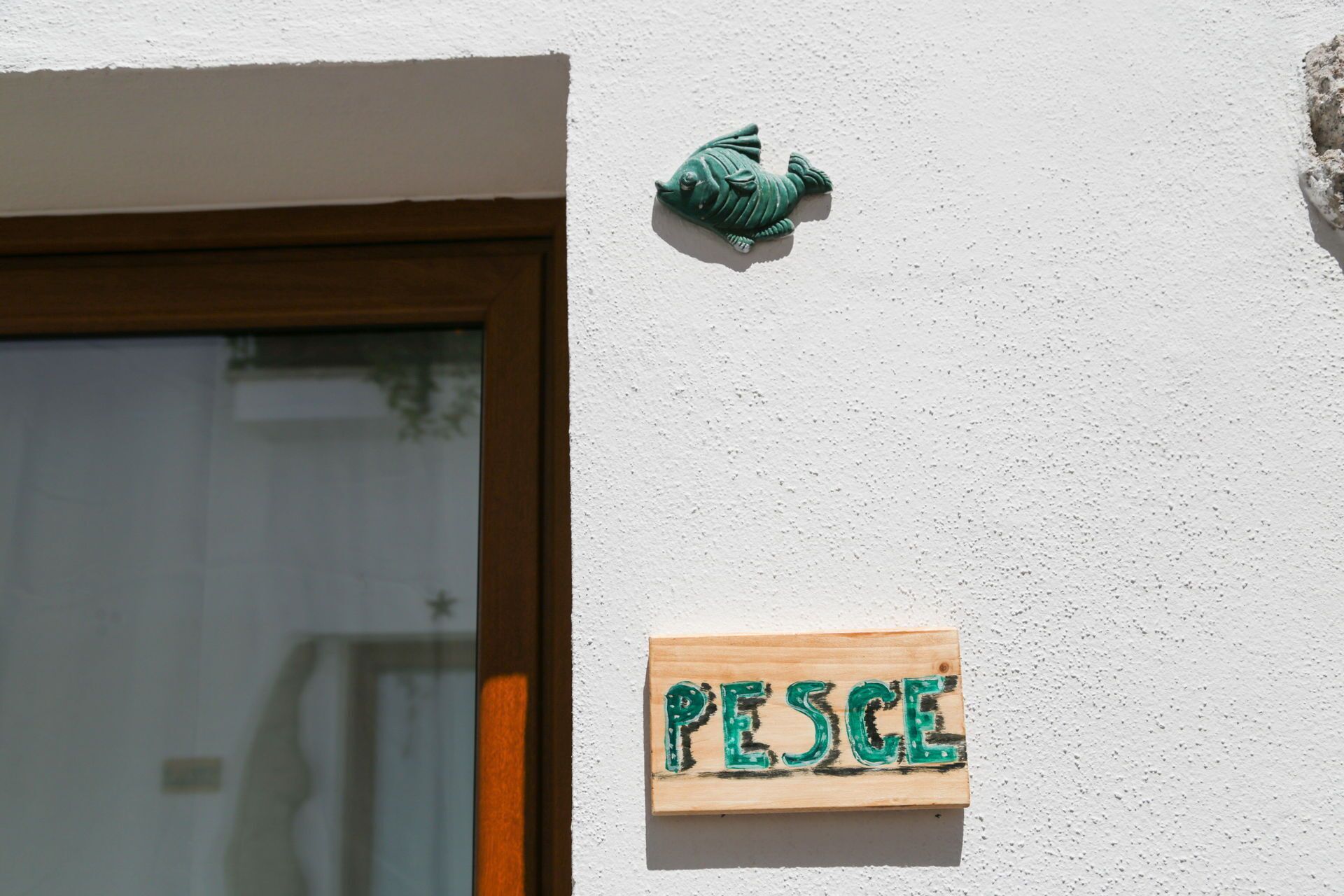Une plaque en bois portant le mot « PESCUE » est fixée à un mur blanc.