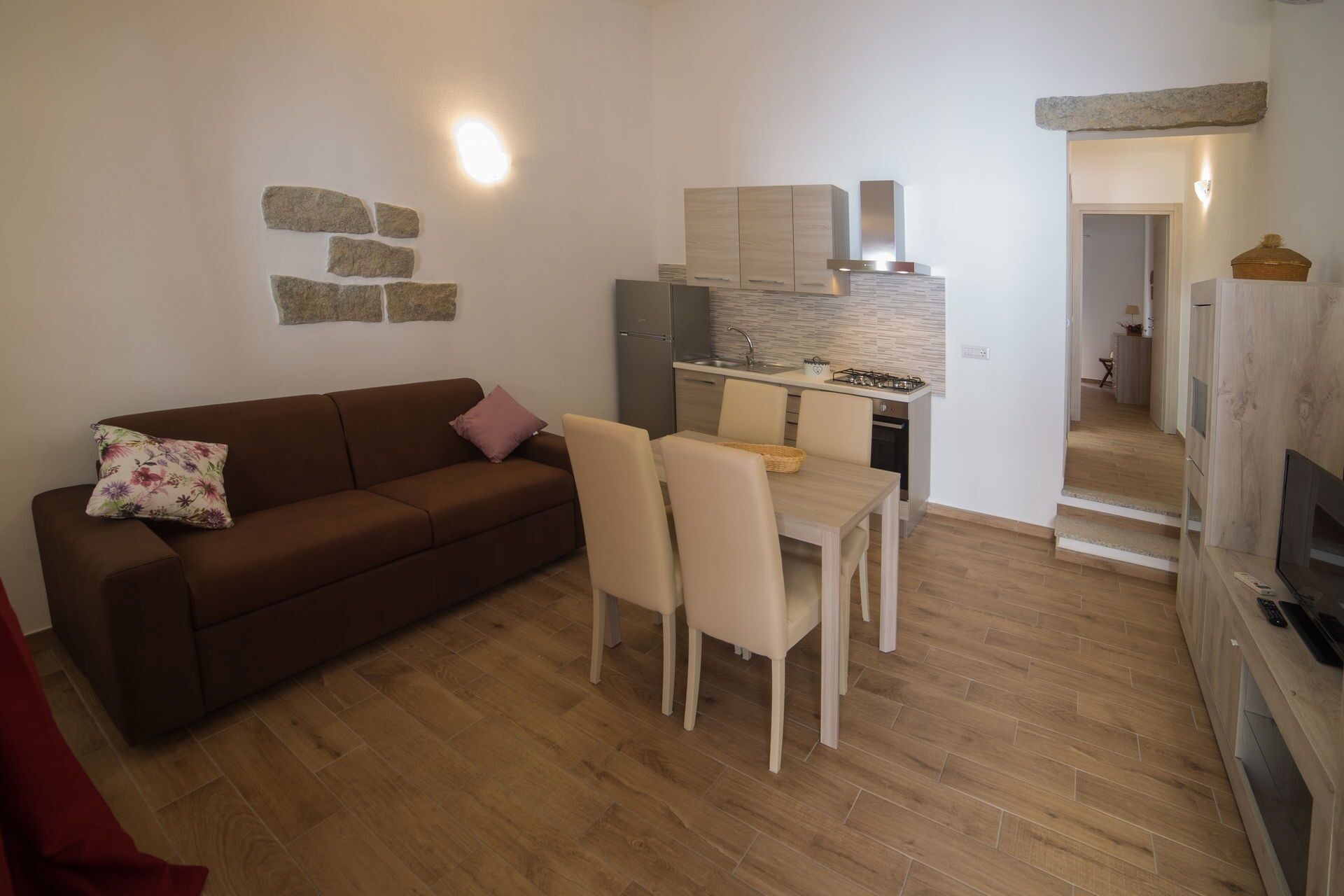 Un espacio habitable compacto con sofá, mesa de comedor y sillas. Se observa una zona de cocina con electrodomésticos modernos y un revestimiento de piedra.