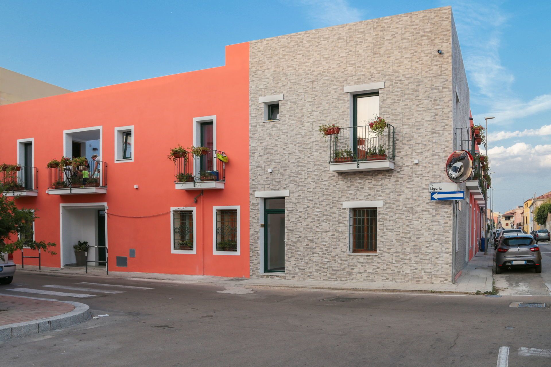 Une vue de rue avec un immeuble doté de balcons ornés de plantes en pot, un ciel dégagé et une enseigne indiquant « Ligurie ».