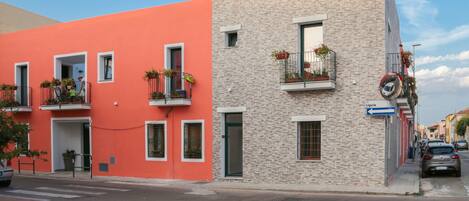 Une vue de rue avec un immeuble doté de balcons ornés de plantes en pot, un ciel dégagé et une enseigne indiquant « Ligurie ».