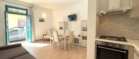 A compact kitchen with a gas stove and oven, a dining area with a table and chairs, and a sofa in the foreground.