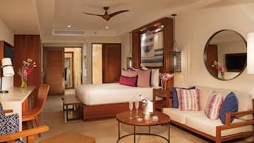 A hotel room with a bed, a sofa, a dining table, and a coffee table. There is a ceiling fan, a mirror, and a TV.