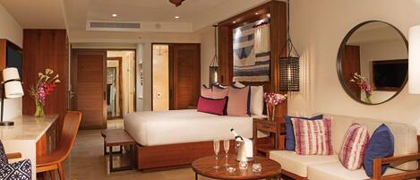 A hotel room with a bed, a sofa, a dining table, and a coffee table. There is a ceiling fan, a mirror, and a TV.