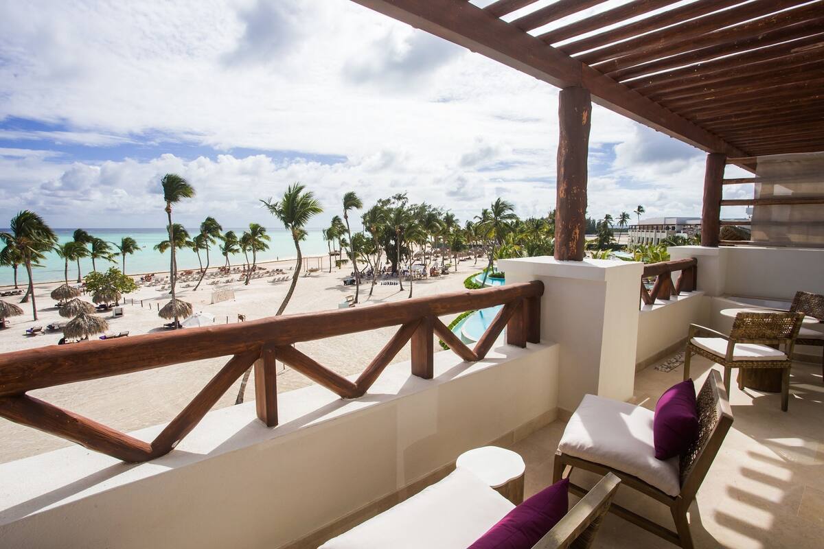 A balcony with a view of a beach, palm trees, and a pool.