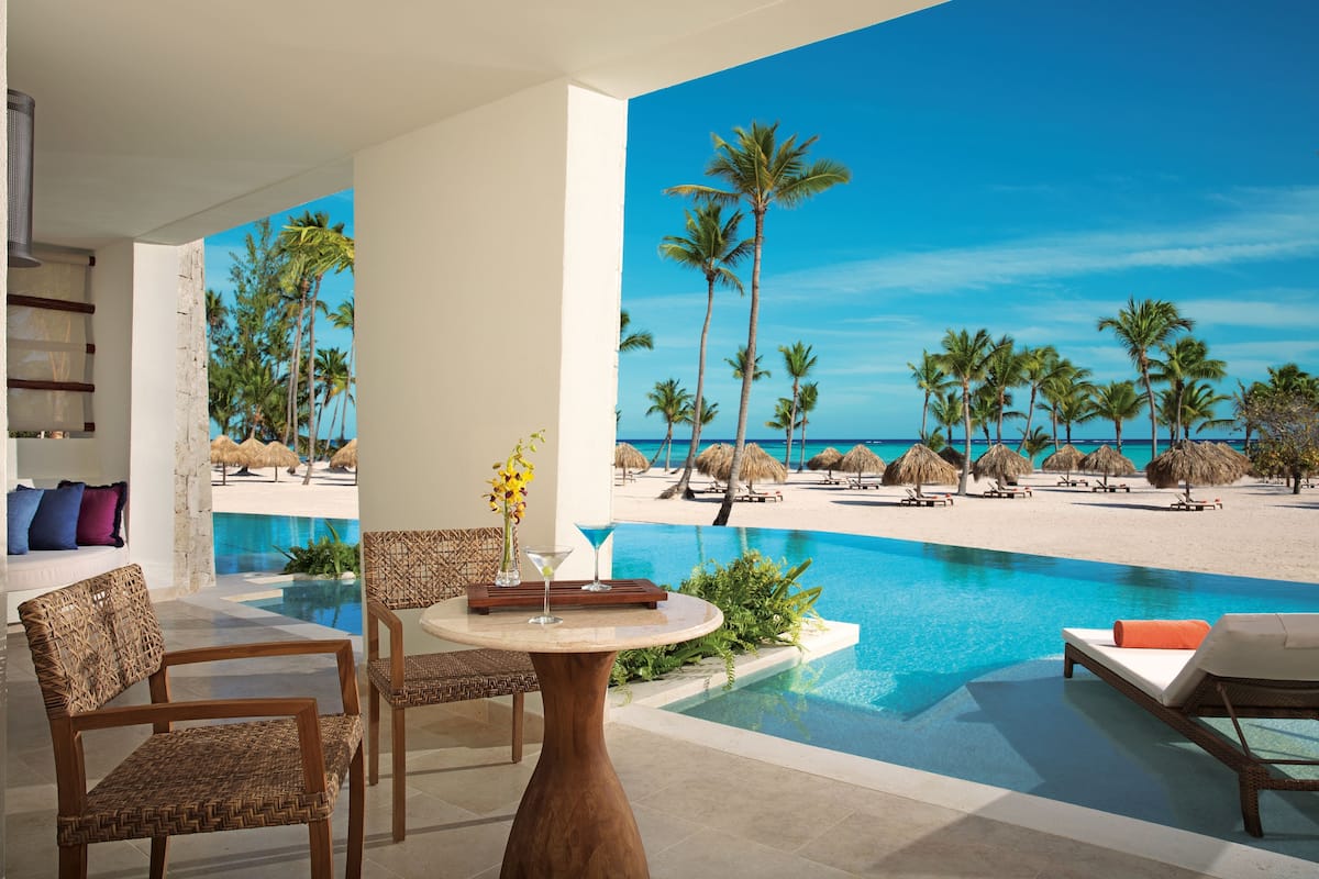 A poolside area with lounge chairs, a table with a vase and drinks, and a view of the beach and ocean.