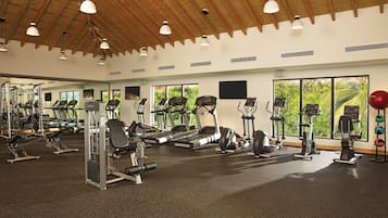A gym with various exercise equipment, large windows, and a high ceiling.