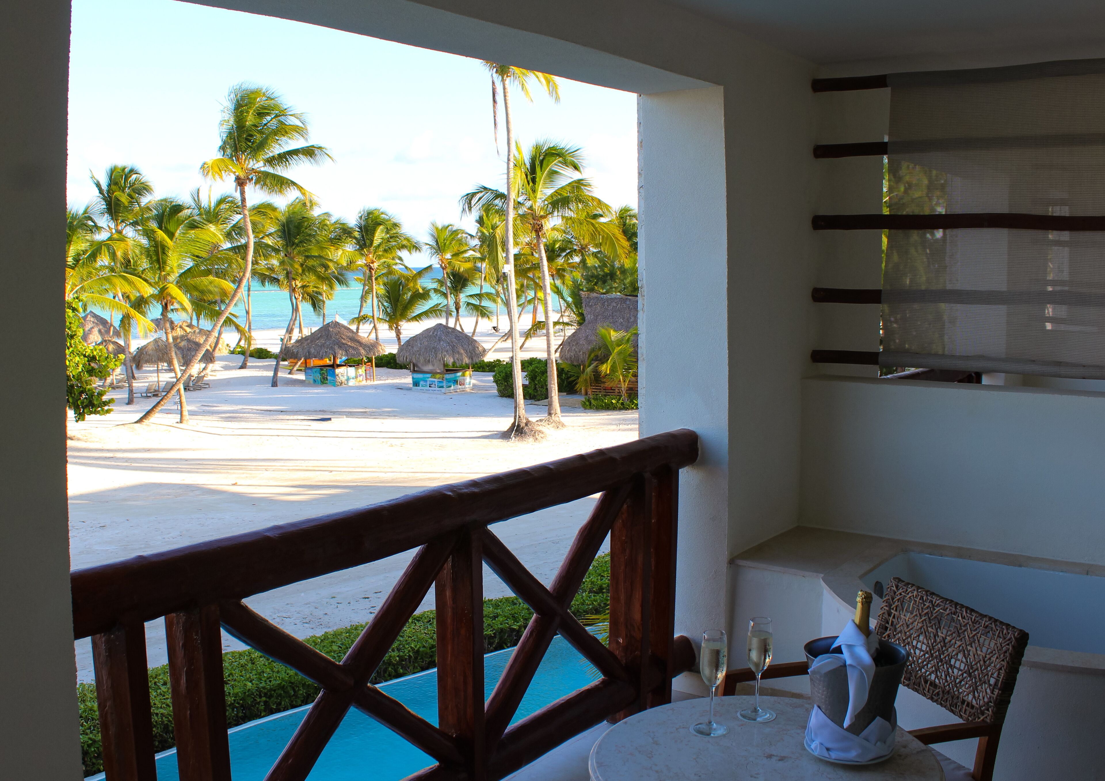 Un balcón con vista a una playa, palmeras y una piscina.