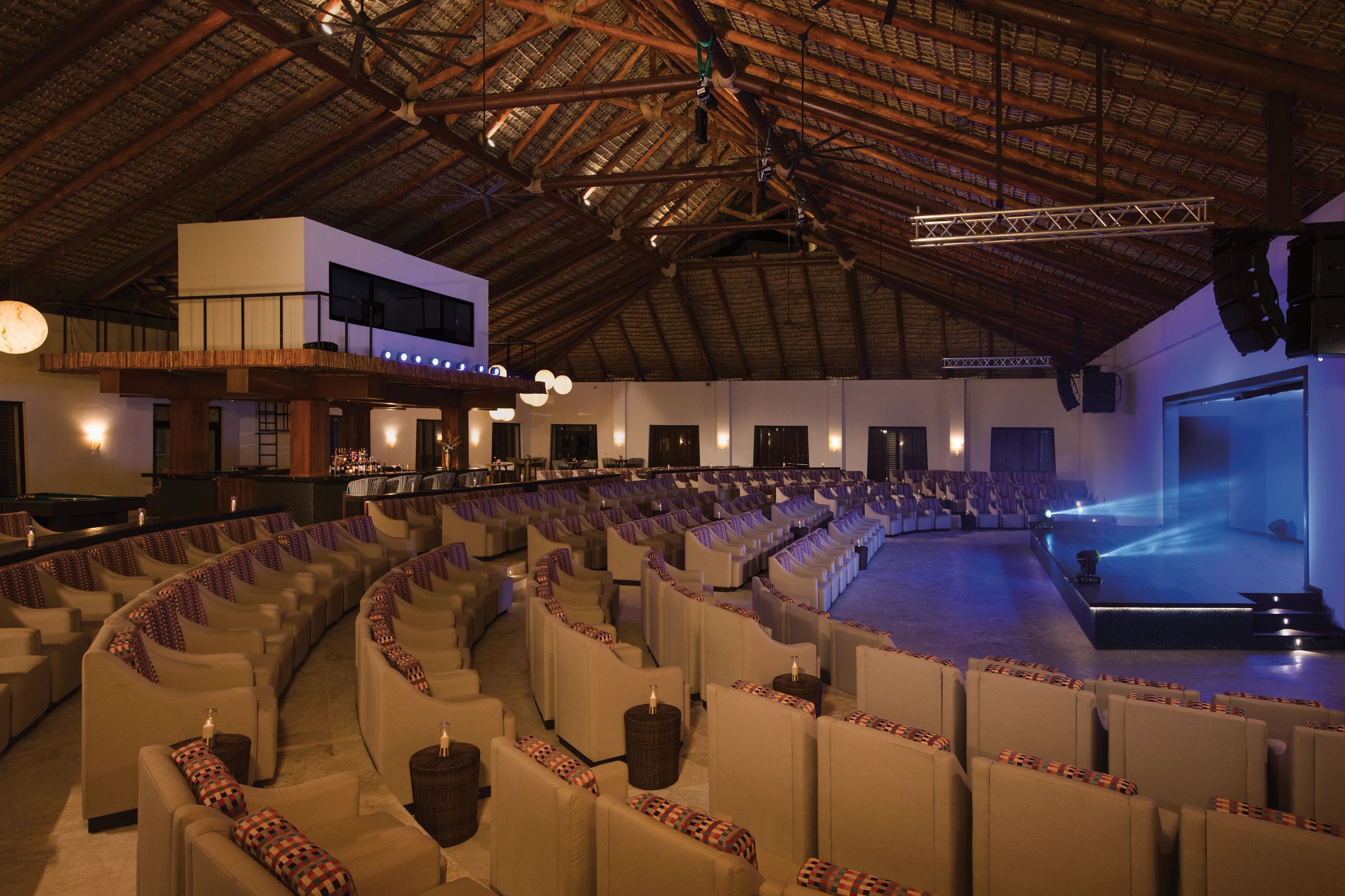 Un auditorium intérieur doté de gradins, d’une scène et d’un plafond recouvert de chaume.