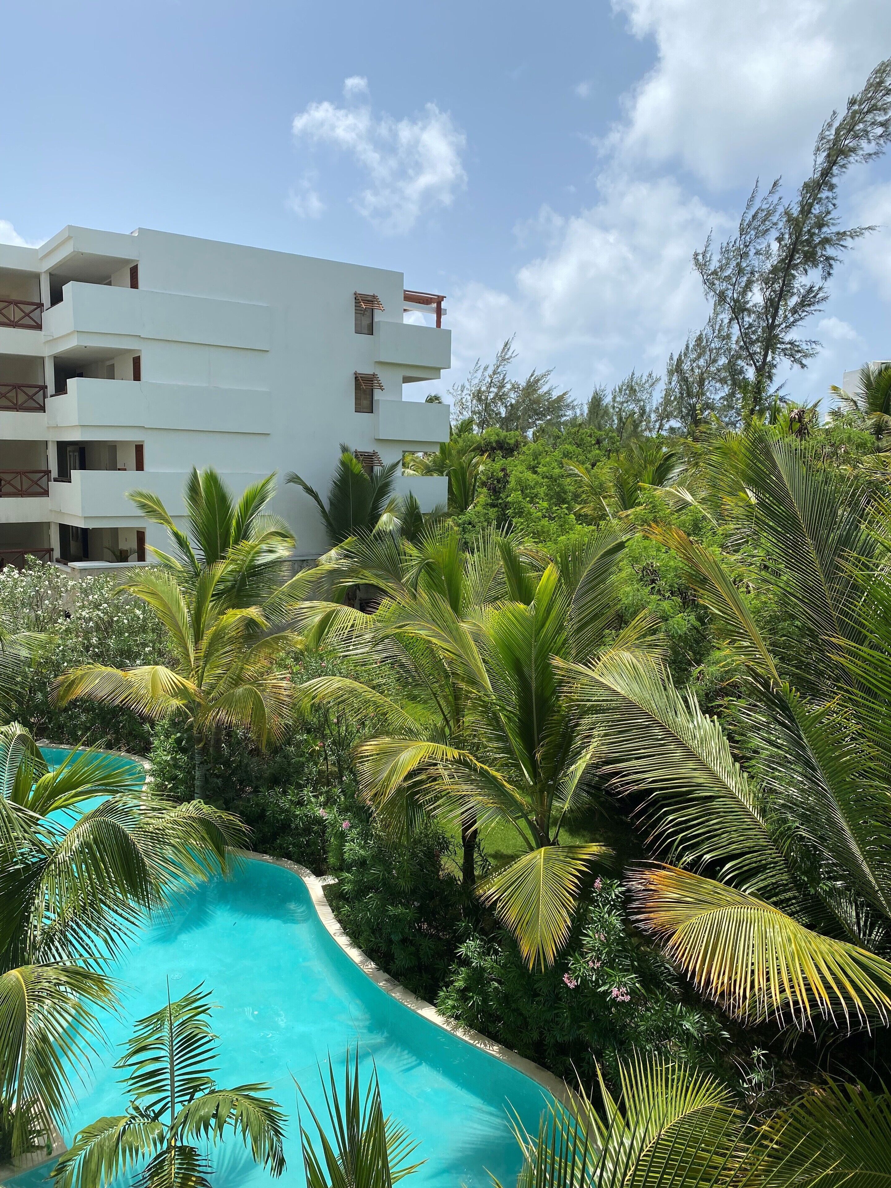 A modern hotel with a pool surrounded by lush greenery and palm trees.
