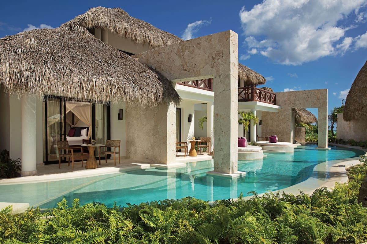 A resort with a swimming pool, thatched-roof structures, and outdoor seating areas.
