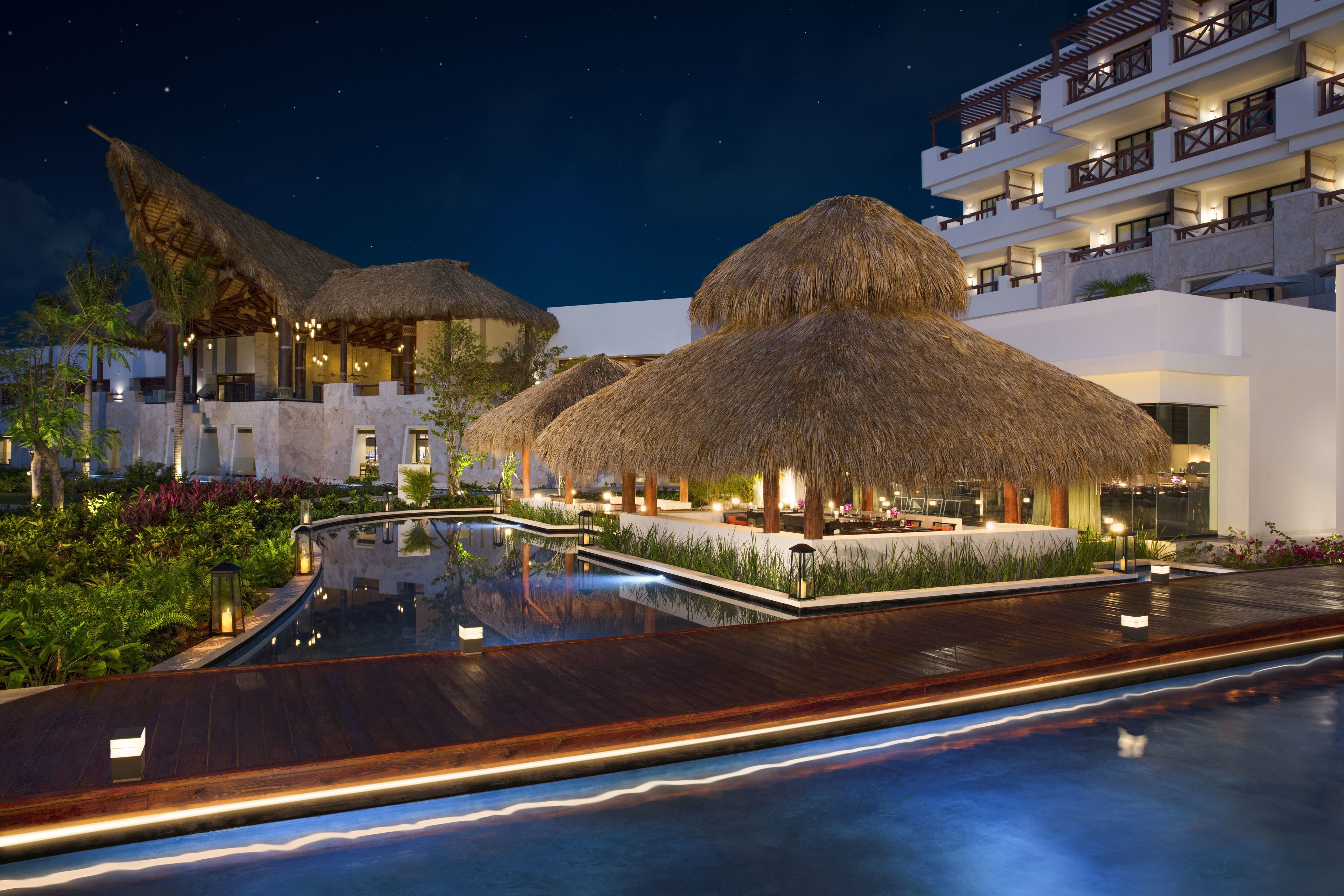 Ein Resort mit strohgedeckten Gebäuden, einem Schwimmbad und einem mehrstöckigen Gebäude mit Balkonen.