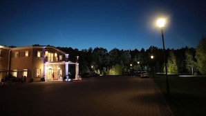A hotel with a paved entrance, a covered outdoor seating area, and a well-lit facade. - Riviera Airport Modlin (OLSZEWNICA NOWA)