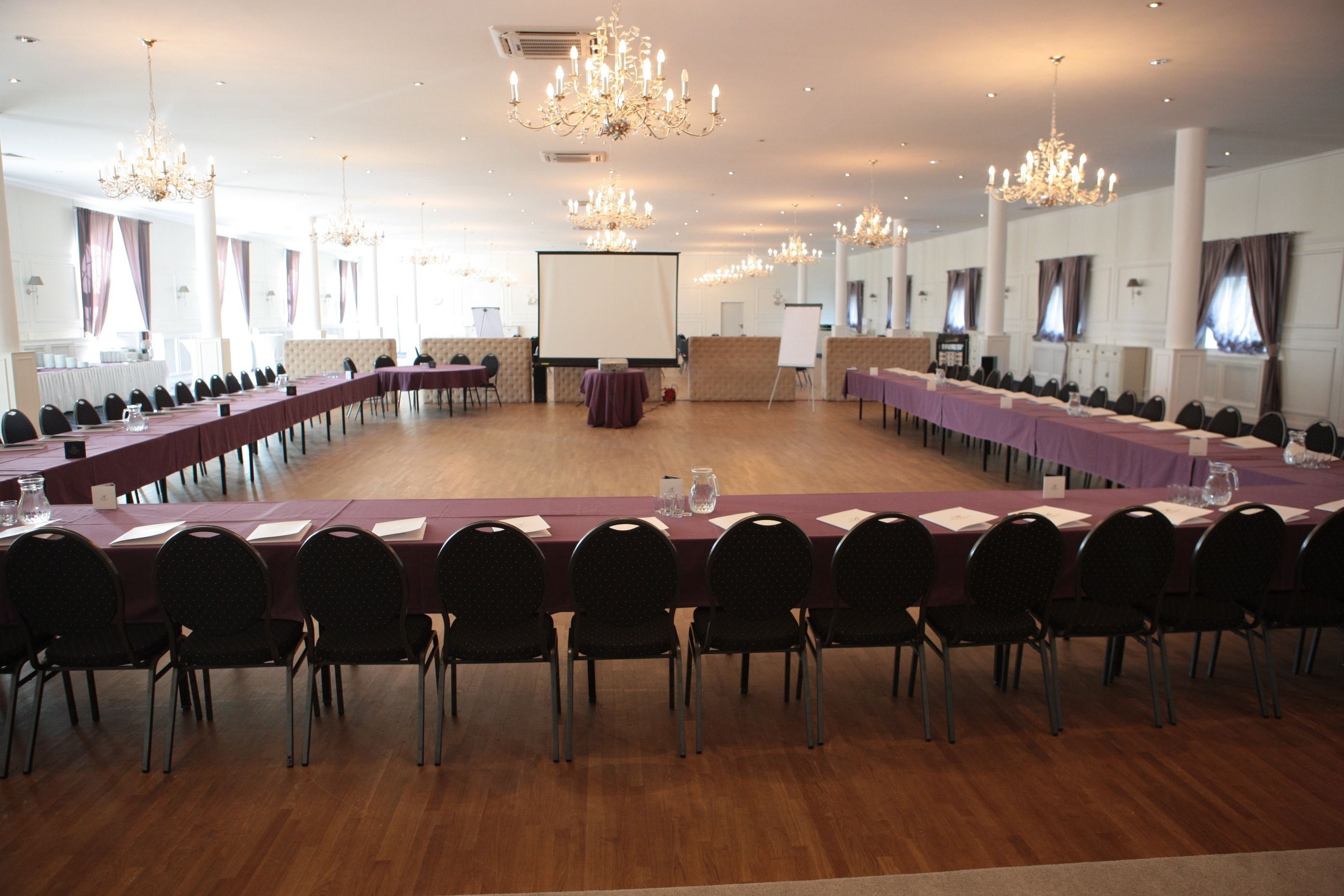 A large conference room with long tables and chairs, chandeliers, and a whiteboard.