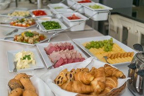 A buffet with various food items including cheese, meats, and pastries.