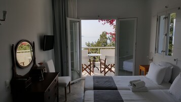 Habitación de hotel con cama, escritorio, silla, televisión y balcón con mesa y sillas.