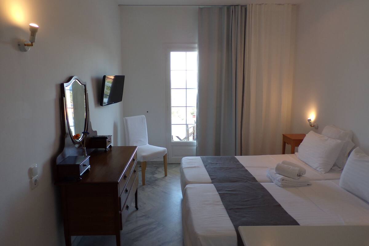 A hotel room with a bed, a desk with a mirror, a television, and a window with curtains.