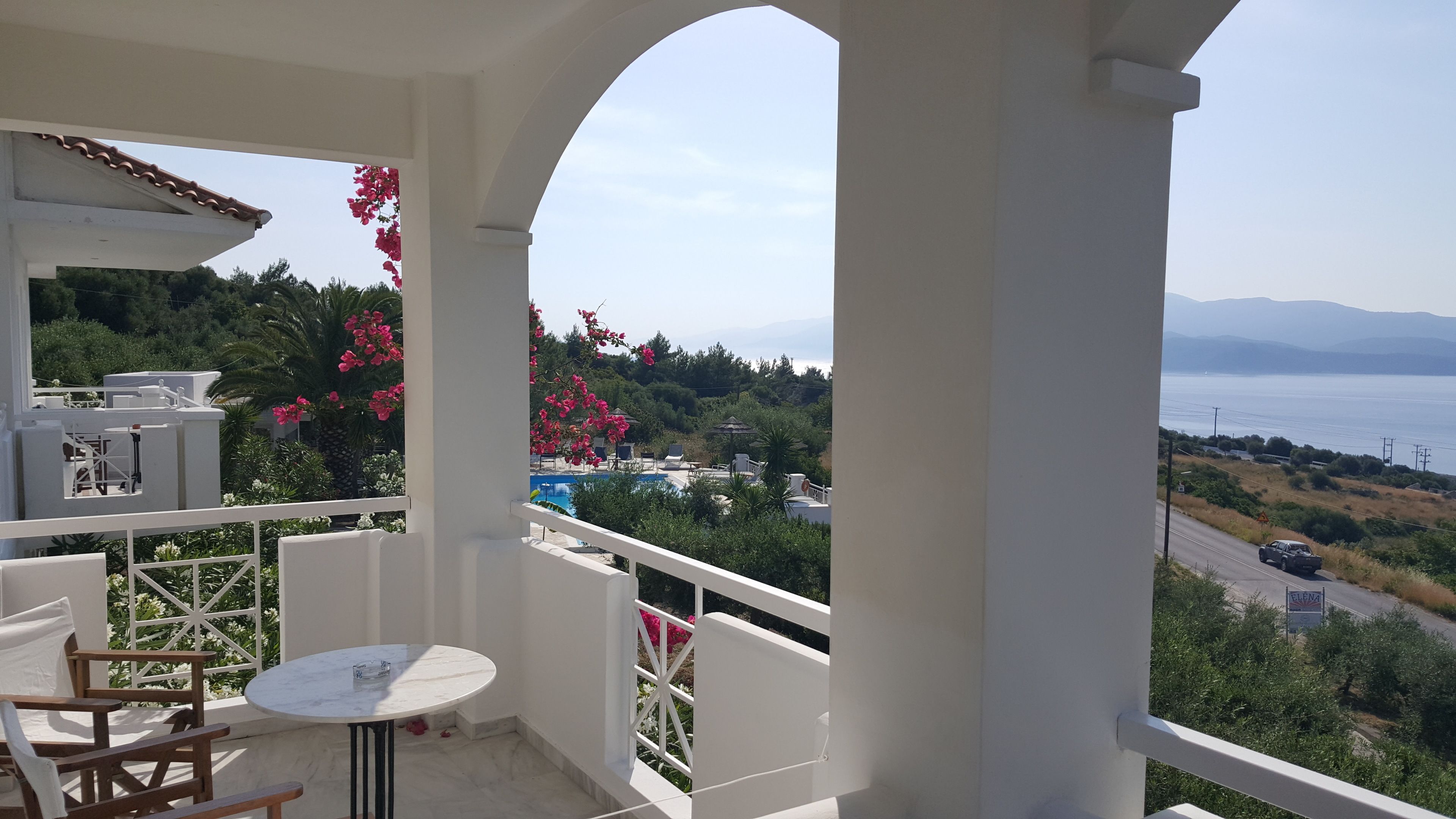Un balcón con mesa y sillas, con vistas a una piscina y abundante vegetación.
