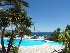 A pool area with lounge chairs and umbrellas, surrounded by palm trees and a view of the sea. - Anthemoessa Villas (Samos)