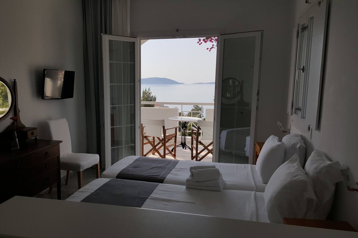 A hotel room with a bed, a desk, a chair, a TV, and a balcony with a table and chairs.