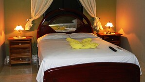 A neatly made bed with a wooden headboard, two bedside tables with lamps, and a window with curtains. - Hotel Rio Guayas (Guayaquil)