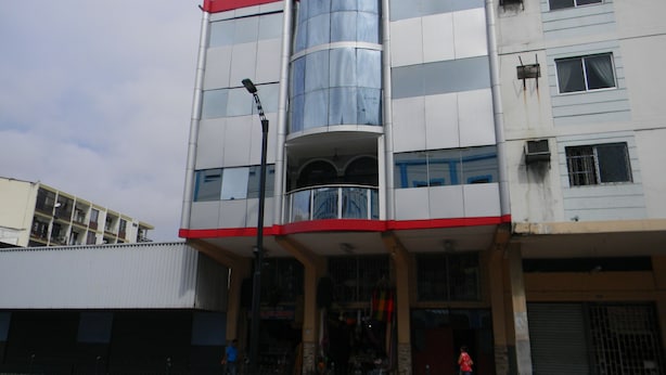 A multi-story building with a central glass elevator shaft, a red and white facade, and a ground-level entrance with a metal gate. - Hotel Rio Guayas (Guayaquil)