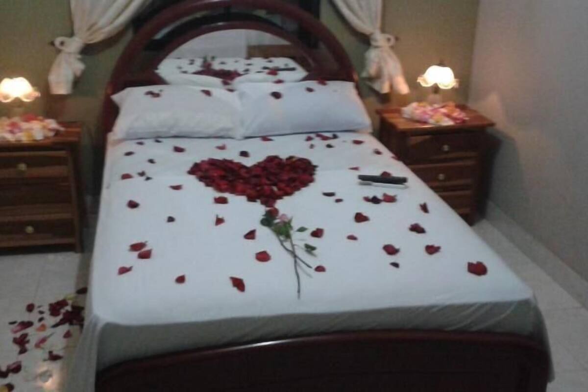 A neatly made bed with a heart-shaped flower arrangement on the bedspread, flanked by two bedside tables with lamps.