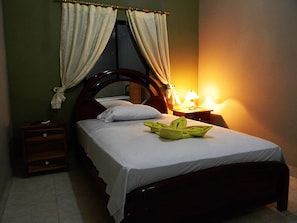 A neatly made bed with a white sheet and pillows, a bedside table with a lamp, and a wooden headboard. - Hotel Rio Guayas (Guayaquil)