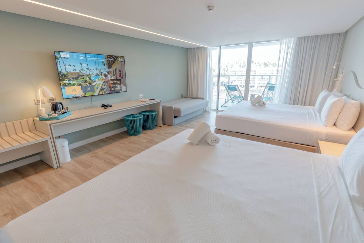 Een moderne hotelkamer met een groot bed, een slaapbank, een aan de muur bevestigde televisie en een balkon met uitzicht.