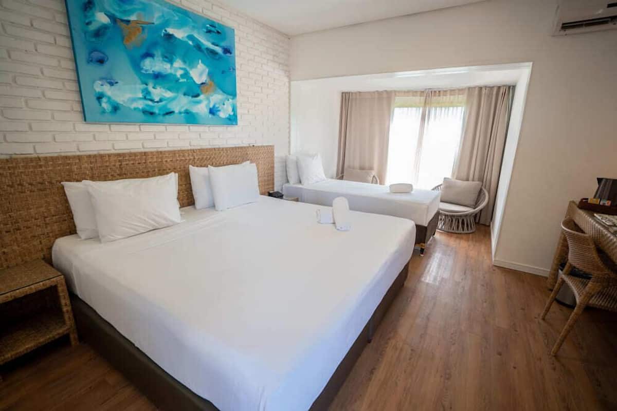 Een hotelkamer met een groot bed, een kleiner bed, een zithoek en een schilderij aan de muur.